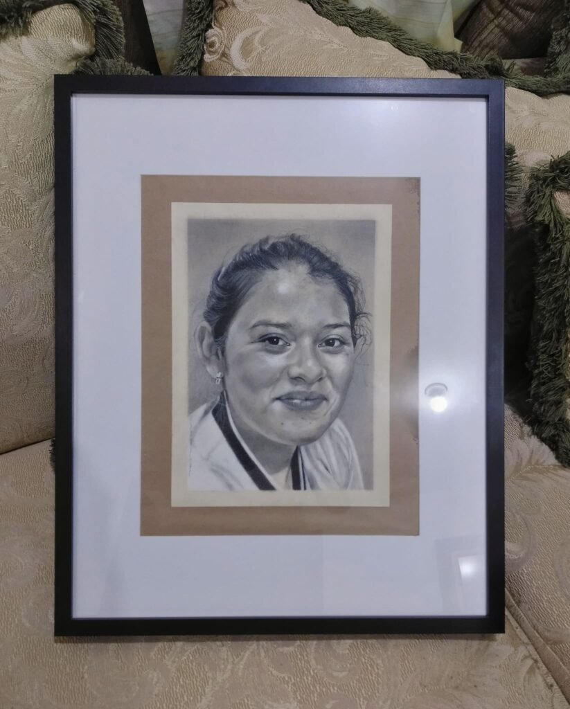 Retrato realista a carboncillo de mujer joven sonriente, obra enmarcada en escala de grises